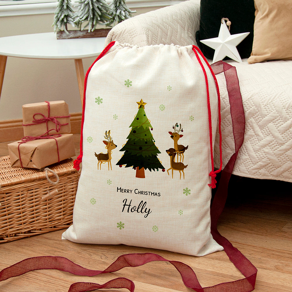 Personalised Christmas sack with reindeer and a Christmas tree, red drawstrings and the name Holly, beside wrapped gifts.